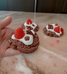 a hand holding some cookies with cream and strawberries on top