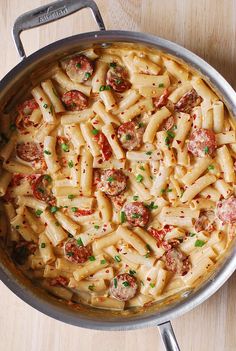 a pan filled with pasta and sausages on top of a wooden table next to utensils