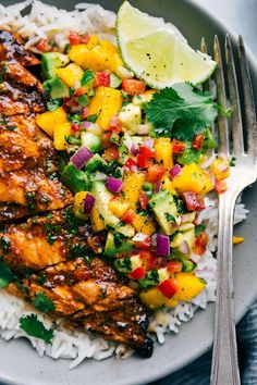 a white plate topped with chicken, rice and pineapple salsa next to a fork