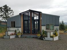 a tiny house made out of shipping containers on gravel with potted plants in the foreground