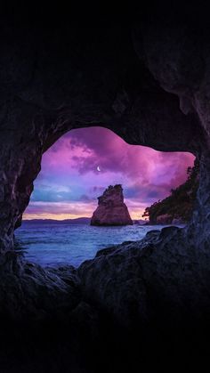 an ocean cave at sunset with the moon in the sky and purple clouds above it