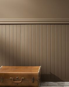 an old suitcase sitting on the floor in front of a wall with wood paneling