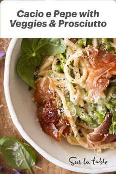 a white bowl filled with pasta and meat on top of a wooden table next to flowers