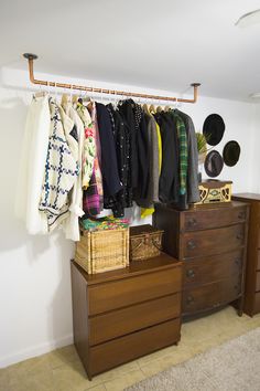 a closet with clothes and hats hanging on the wall next to a dresser in front of a mirror