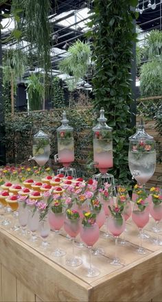 a table topped with lots of wine glasses filled with pink liquid and flowers in vases