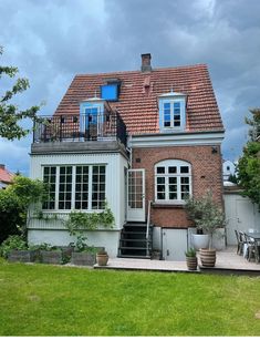 a house with a red brick roof and white windows on the top floor is surrounded by green grass