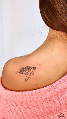 a woman with a turtle tattoo on her back shoulder and behind her neck is a pink sweater