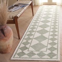 a white and green area rug in a living room next to a wooden table with a vase on it