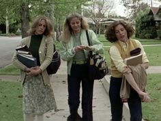 three women are standing on the sidewalk looking at something