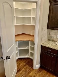 an empty pantry in the corner of a kitchen with wood floors and cabinets on either side