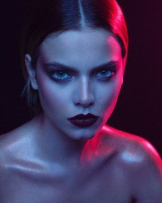 a woman with red light on her face and blue eyes, posing for the camera