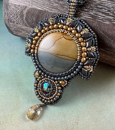 a brown and black beaded necklace with an oval stone in the center on a wooden surface