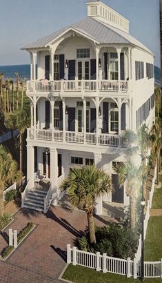 an aerial view of a large white house with palm trees in the foreground and ocean in the background