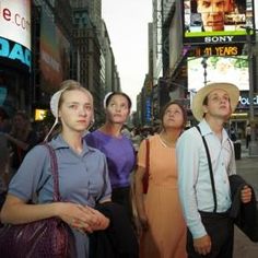 a group of people standing on the side of a street next to each other in front of tall buildings