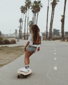 a woman riding a skateboard down the middle of a road next to palm trees