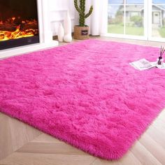 a bright pink area rug is in front of a fire place with a plant on the floor