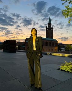 a woman standing on the sidewalk in front of a building with a clock tower behind her