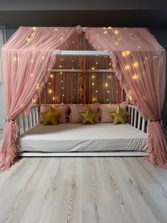 a pink canopy bed with stars on the pillows and lights hanging from it's sides