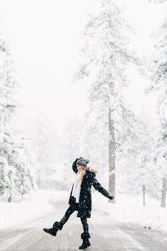 a woman walking across a snow covered road in the middle of winter with her arms outstretched