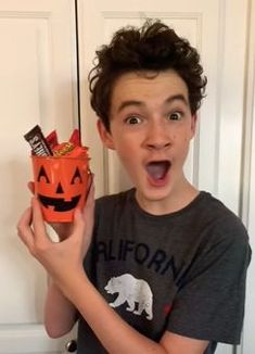 a young man holding an orange candy box with a jack - o'- lantern on it