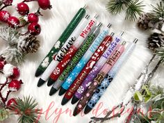 christmas themed pens are lined up on a white fur covered surface with pine cones and evergreen branches in the background