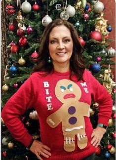 a woman standing in front of a christmas tree wearing a sweater with a ginger on it