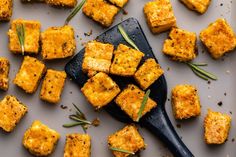 tofu cubes on a black spoon with rosemary sprigs and seasoning