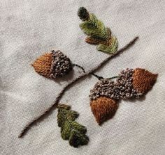 three embroidered leaves on a white piece of cloth with brown and green thread, sitting next to each other