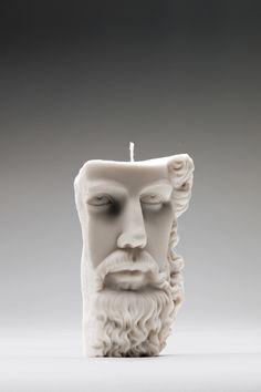 a white candle with a face and beard on the top, in front of a gray background