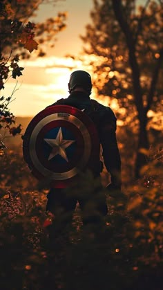 a man with a captain america shield standing in the woods looking at the sun set