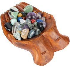 a wooden bowl filled with lots of different colored rocks on top of a white background