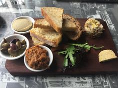 a wooden cutting board topped with different types of food and dipping sauces on top of it