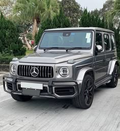 a mercedes g - class is parked in front of some trees and bushes on the street