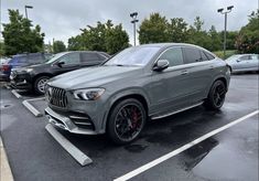 a grey mercedes suv is parked in a parking lot with other cars and trees behind it