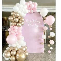 a pink and gold birthday party with balloons, streamers and a large balloon arch