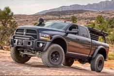 a large black truck parked on top of a dirt road next to trees and mountains