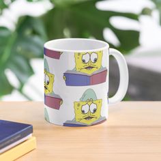 a mug with the faces of cartoon characters on it sitting on a table next to a book