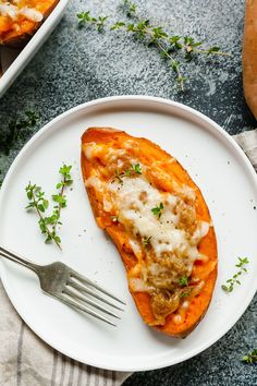 a white plate topped with sweet potatoes covered in cheese and meat, next to a fork