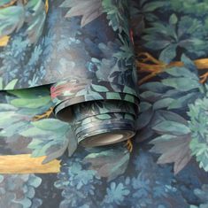 a roll of wrapping paper on top of a flowery wallpaper covered in blue and green leaves