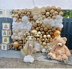 a teddy bear sitting in front of a giant balloon wall with gold and white balloons