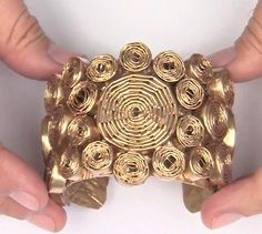 two hands are holding a gold object made out of rolled up rolls of toilet paper