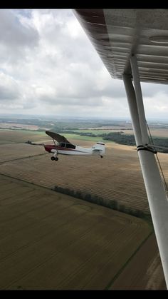 an airplane is flying low over the ground in front of some crops and fields on a cloudy day