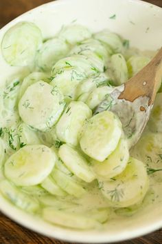 a wooden spoon in a white bowl filled with cucumber slices and dill