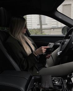 a woman sitting in the driver's seat of a car looking at her cell phone