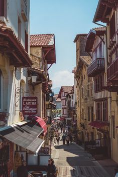 people are walking down the street in an old european town with many buildings and shops