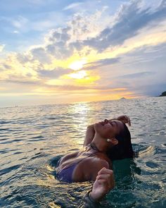 a woman laying on top of a surfboard in the middle of the ocean at sunset