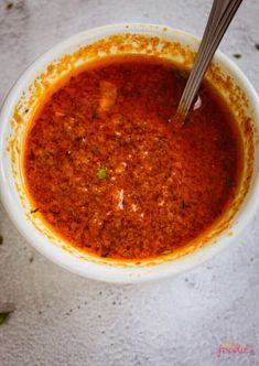 a white bowl filled with red sauce on top of a table next to a spoon