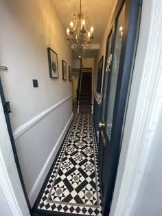 a hallway with black and white tile flooring and chandelier hanging from the ceiling