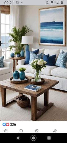 a living room with white couches and blue pillows on the coffee table in front of a painting