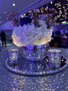 flowers in a disco ball vase on a table with two silver cups and saucers